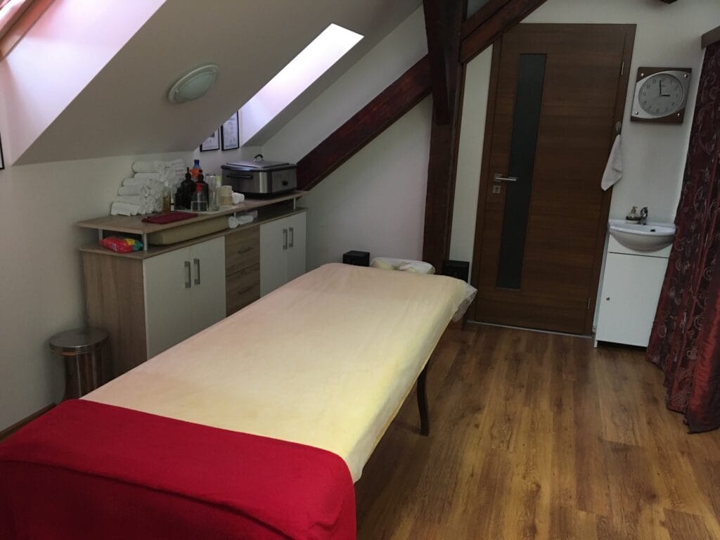 Miestnosť s masážnym stolom a červenou dekou pre profesionálne masáže.