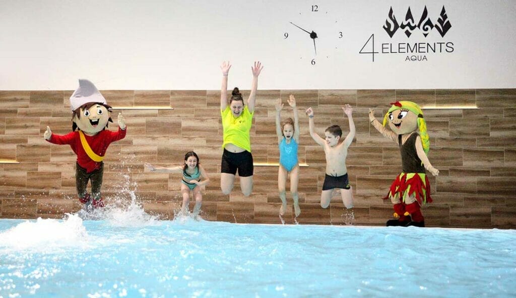 Skupina detí skákajúcich do krytého bazéna s maskotmi vo Wellness centre 4 Elements v hoteli Atrium Nový Smokovec.