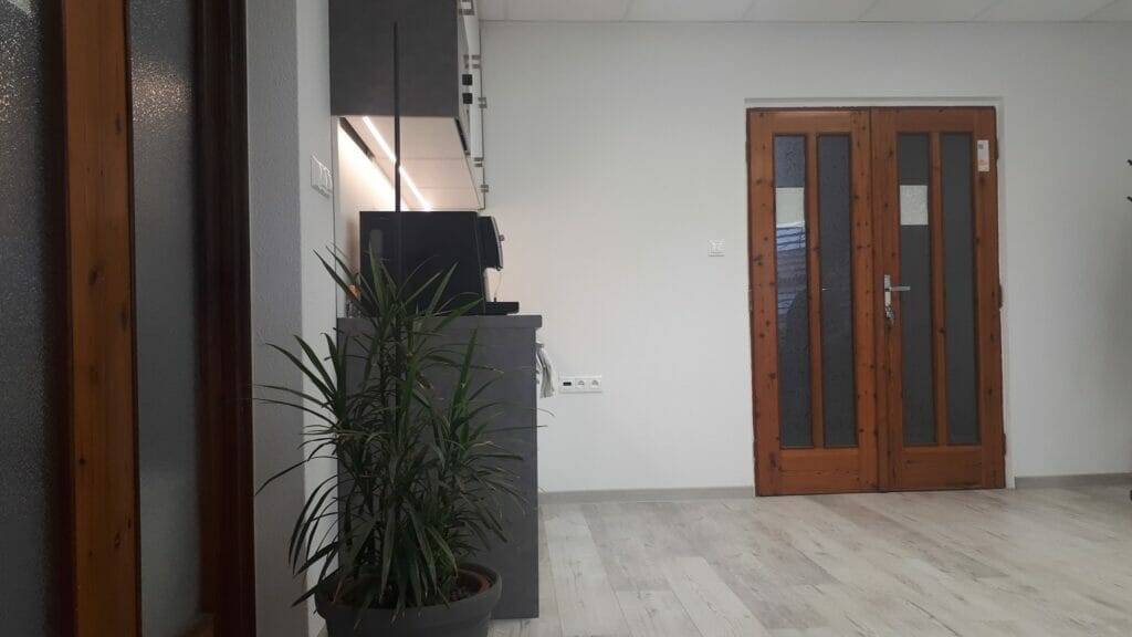 Prázdna kancelária s drevenými dverami a rastlinami v črepníkoch.