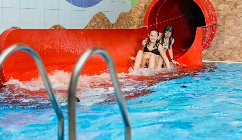 Wellness centrum v hoteli Sitno Vyhne so skupinou ľudí jazdiacich na tobogáne v krytom bazéne.