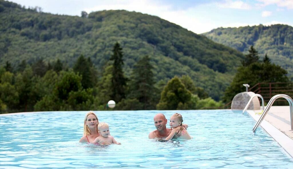 Vo vonkajšom bazéne wellness hotela Sitno Vyhne s horami v pozadí sa pláva rodina.