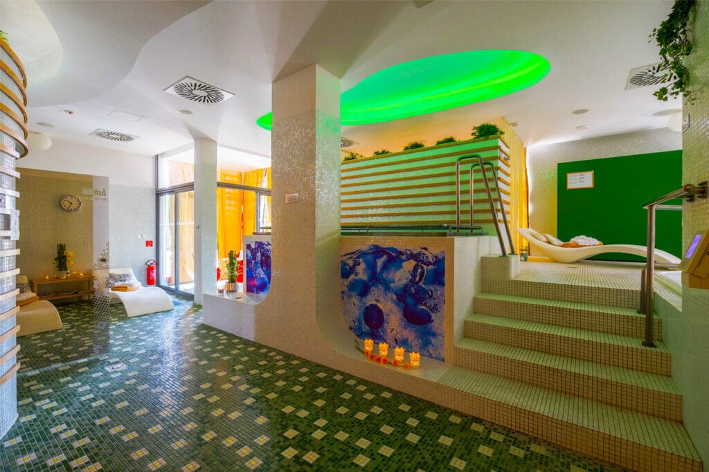 Hotelová kúpeľňa so zelenou dlažbou a zeleným svetlom.