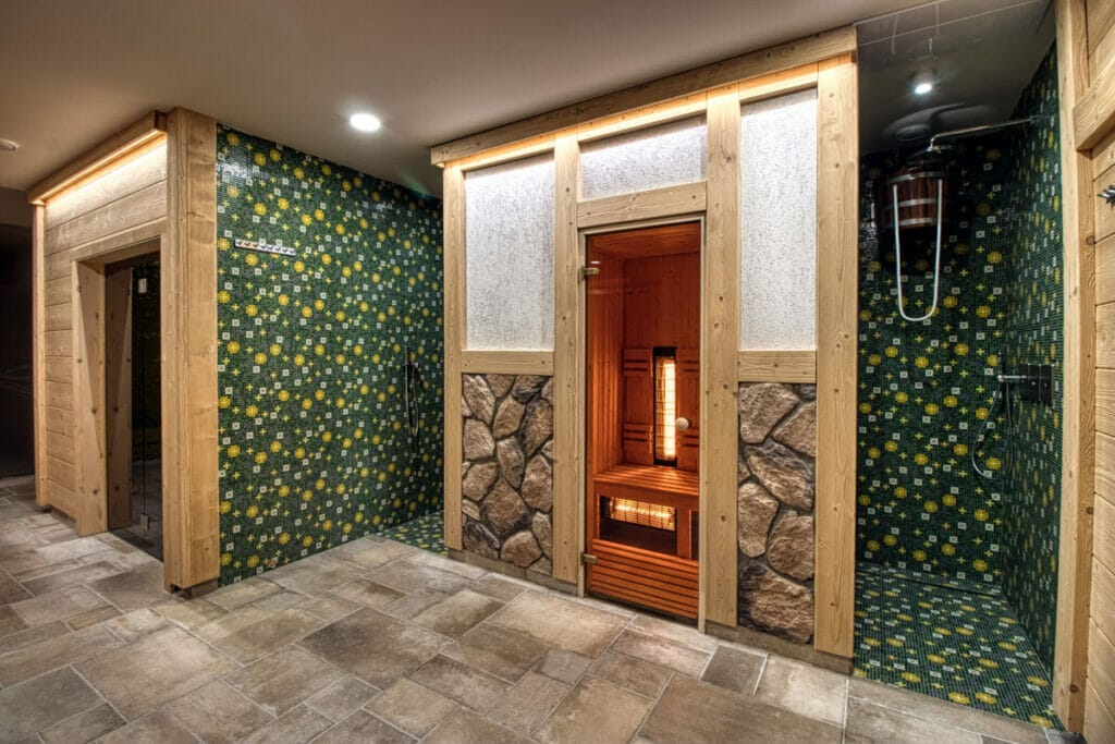 Kúpeľňa so zelenými obkladmi a sprchovacím kútom vo wellness centre v hoteli Familia Stará Ľubovňa.