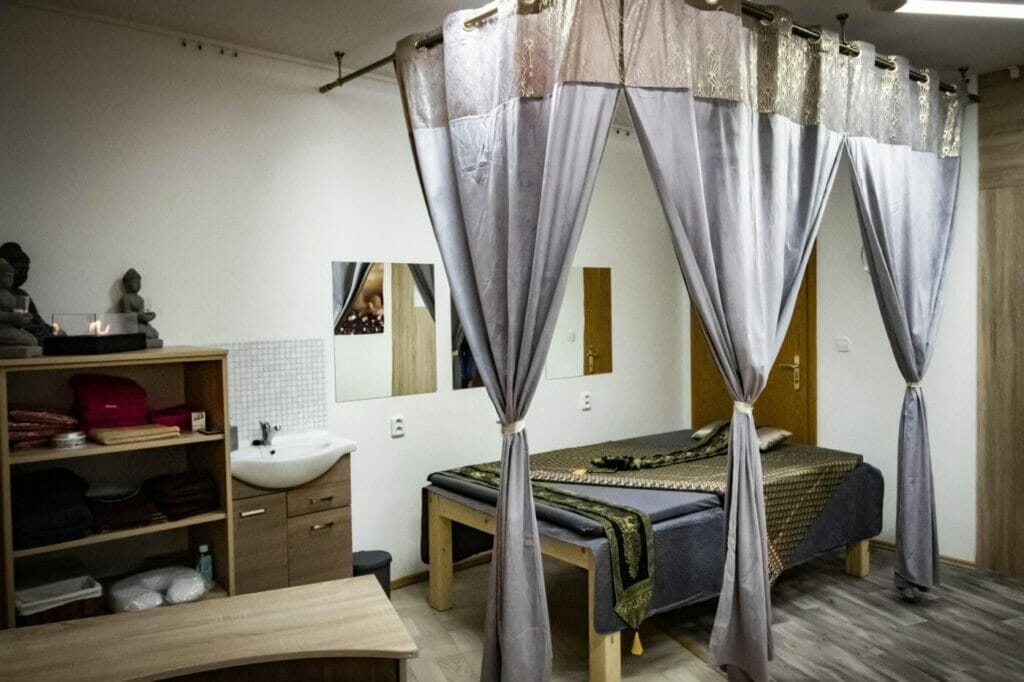 Miestnosť thajských masáží s posteľou a závesmi.