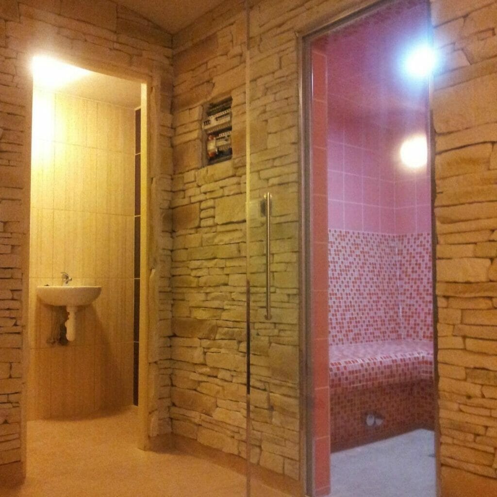 Wellness kúpeľňa so sklenenými dverami a ružovými stenami.