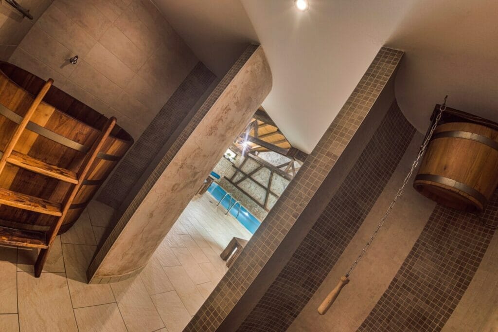 Kúpeľňa v tematike Podolínec s drevenými policami a dreveným sudom.